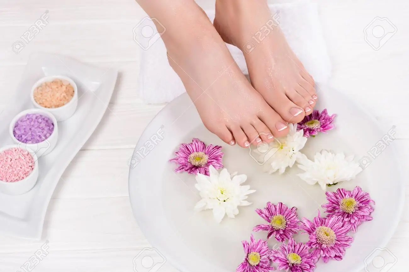 106121100-abgeschnittener-schuss-der-barfußfrau-die-bad-für-nägel-mit-meersalz-und-blumen-im-schönheitssalon-e