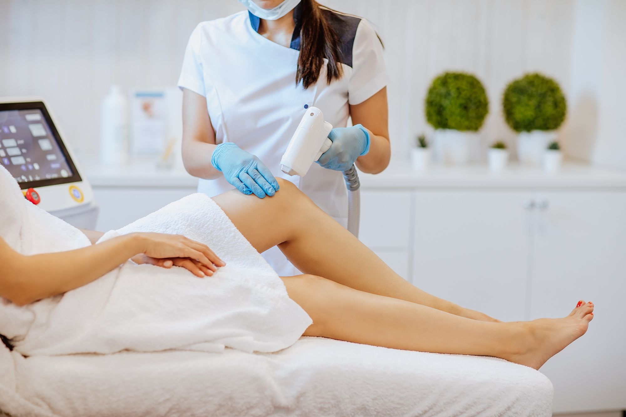 Doctors’s hands in medical gloves using a depilation machine at the woman’s legs